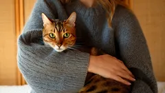 Žena v šedém svetru drží v náručí bengálskou kočku s výraznou srstí.